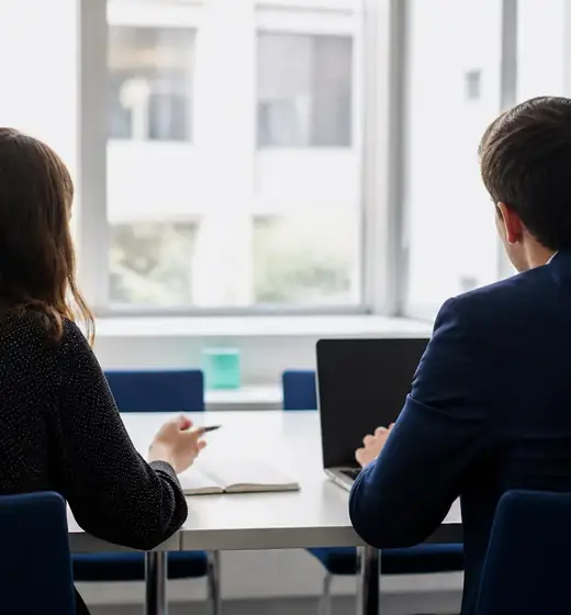 Deux collègues échangent autour d’une table de réunion, vues de dos