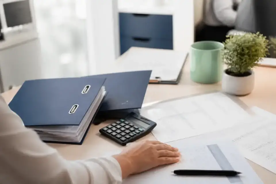 Calculatrice, classeurs indigo et relevés chiffrés sur un bureau clair