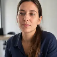 Portrait de Yasmine Kessar, cheveux bruns attachés, chemise bleu indigo, près d’une fenêtre